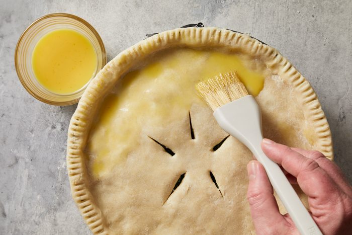Overhead shot of a small bowl whisk remaining egg and 1 tablespoon water; brush over crust; Bake until crust is golden brown and a knife inserted in center comes out clean; about 1 hour; Serve warm or at room temperature; marble surface;