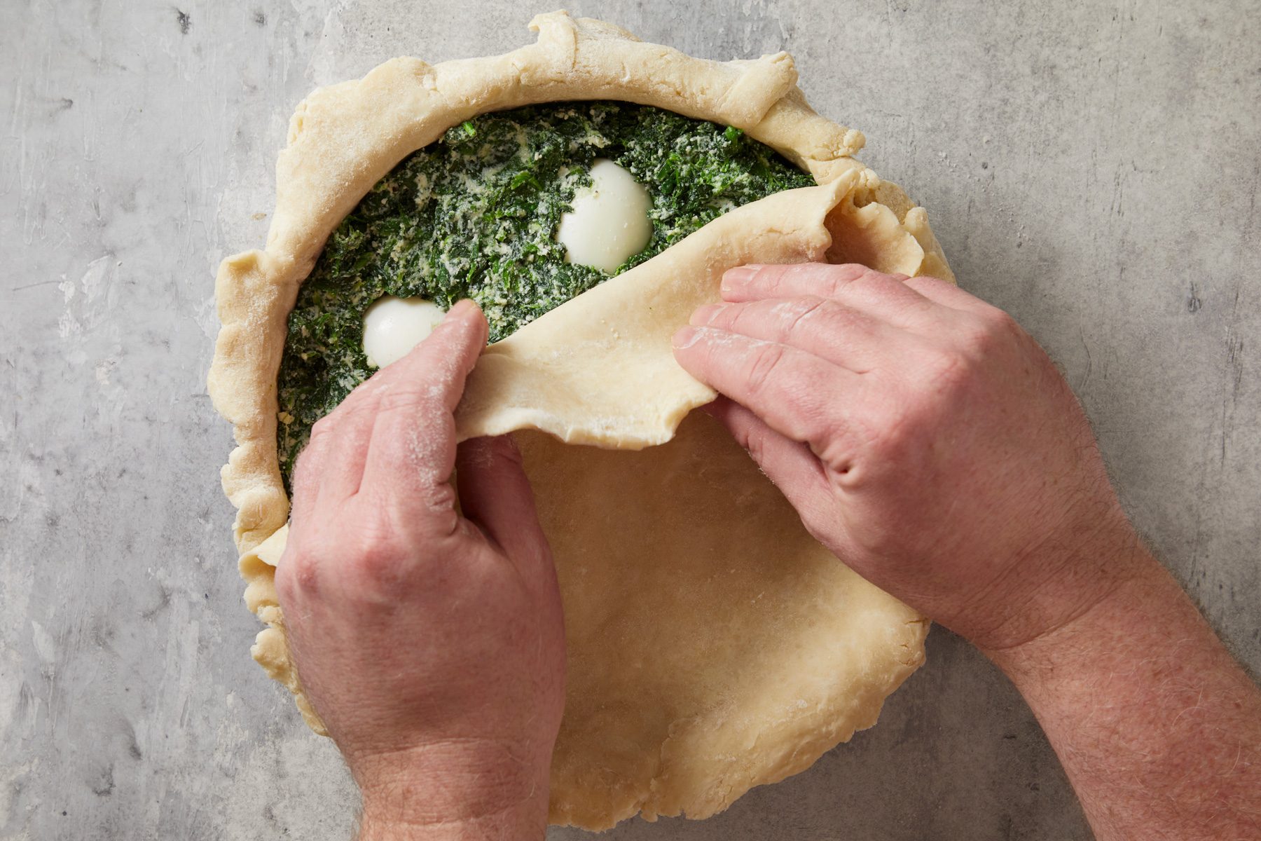 Overhead shot of roll remaining dough to an 11-inch circle and place over filling; Trim and seal edge; cut five slits in top; marble surface;