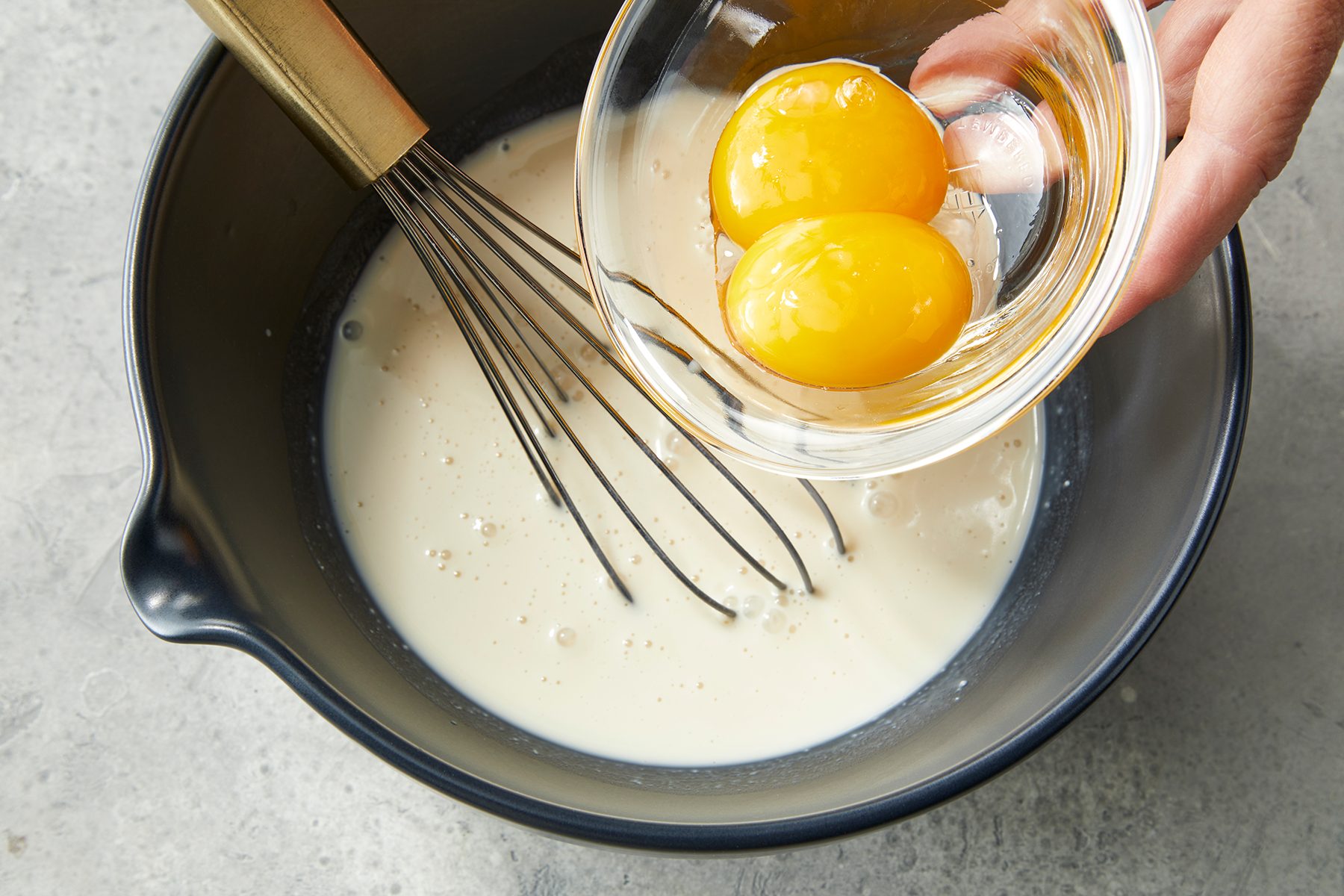 A mixing bowl contains a whisk and a creamy liquid batter. 
