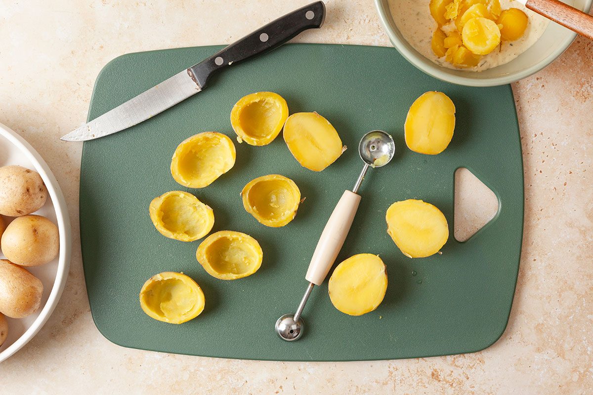 Half length boiled potatoes being scooped on a board