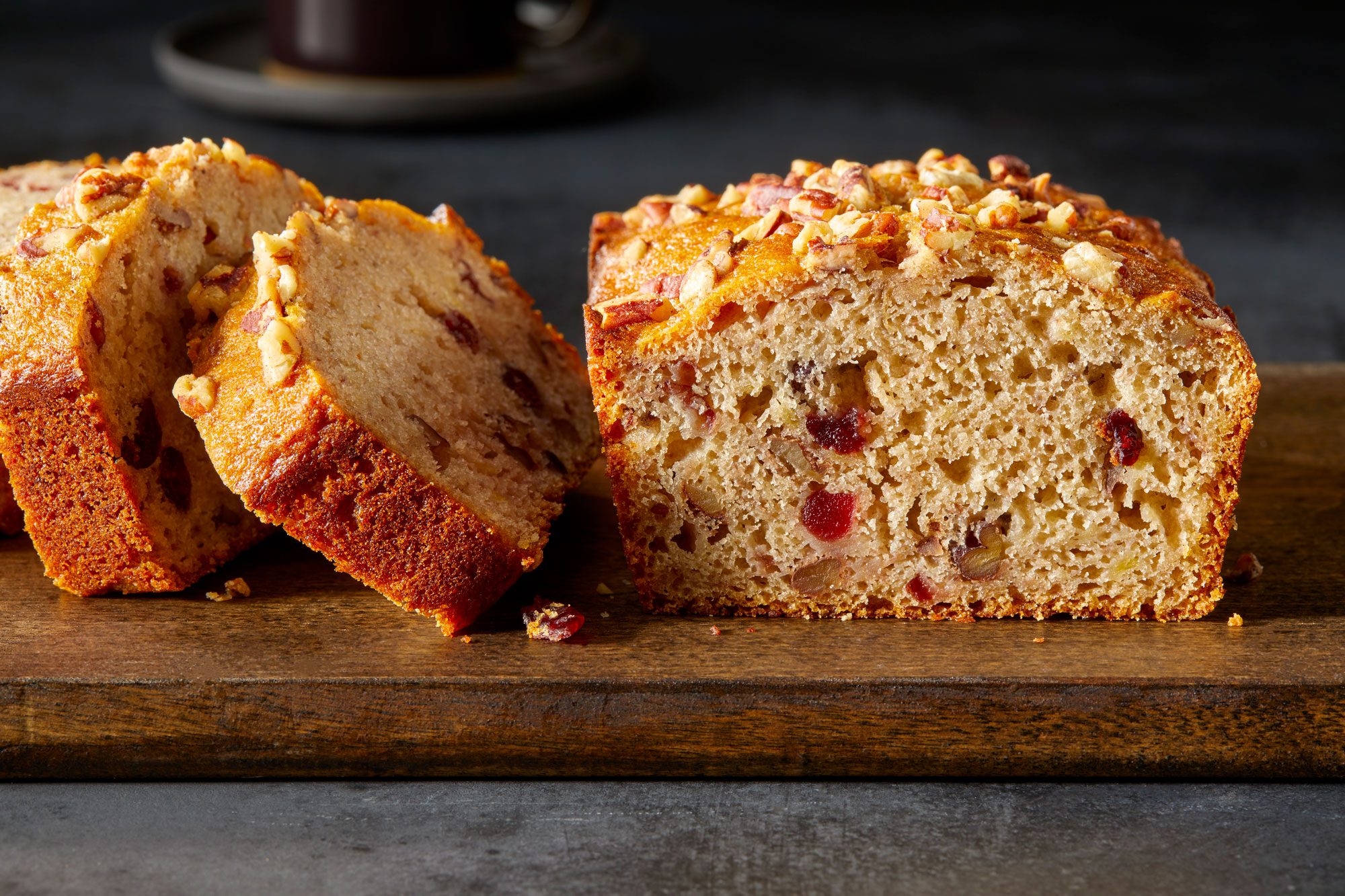 Close view shot of Double Cranberry Banana Bread; cut into slices and served on wooden tray; dark surface;