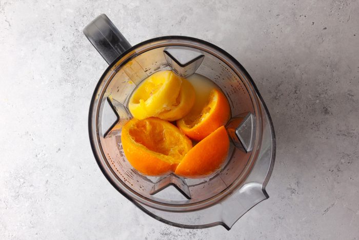 overhead shot of a blender pitcher is filled with several pieces of oranges; the background features a light gray surface