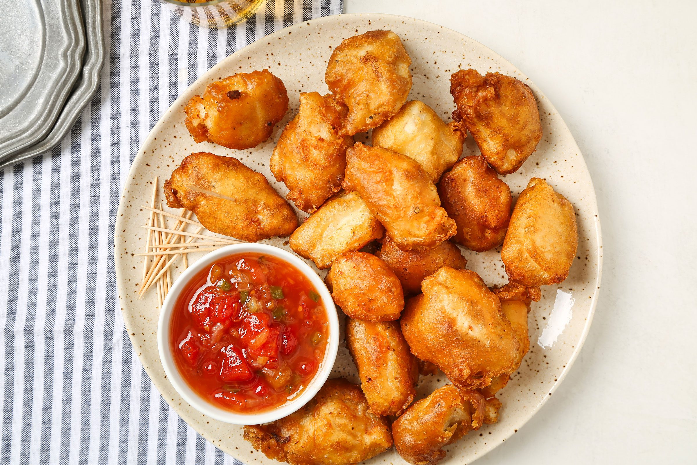 Fried Sweet And Sour Chicken in a cream plate on a striped kitchen towel with a sauce on side