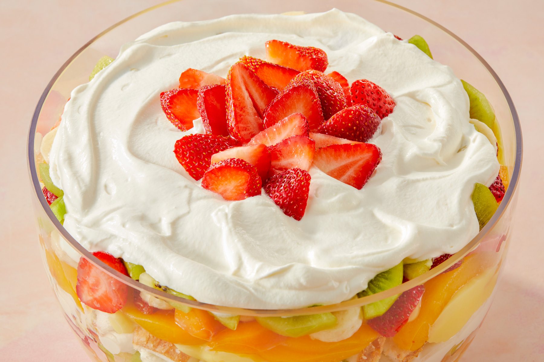 3/4th shot of Fruit Trifle in a clear glass bowl; it is layered with an assortment of fruits and creamy whipped topping