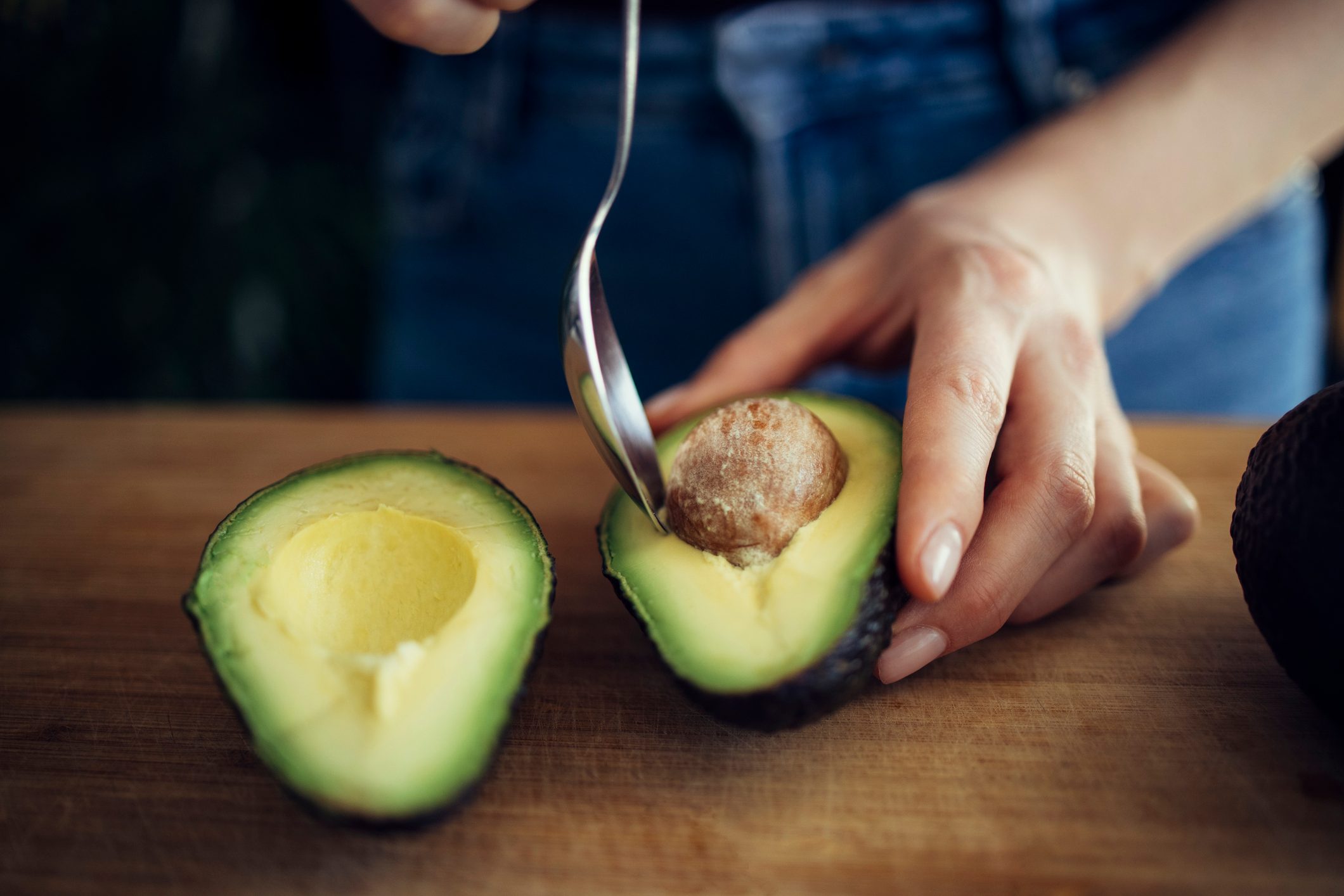 Close Up Photo of Woman Removing Seed from Avocado Half with Spoon