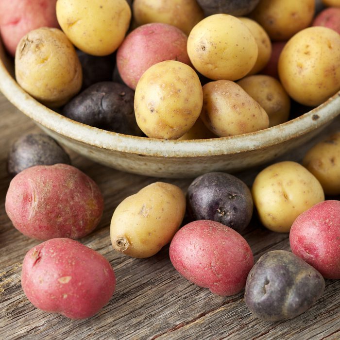 Raw multi-colored small potatoes in ceramic bowl on wood