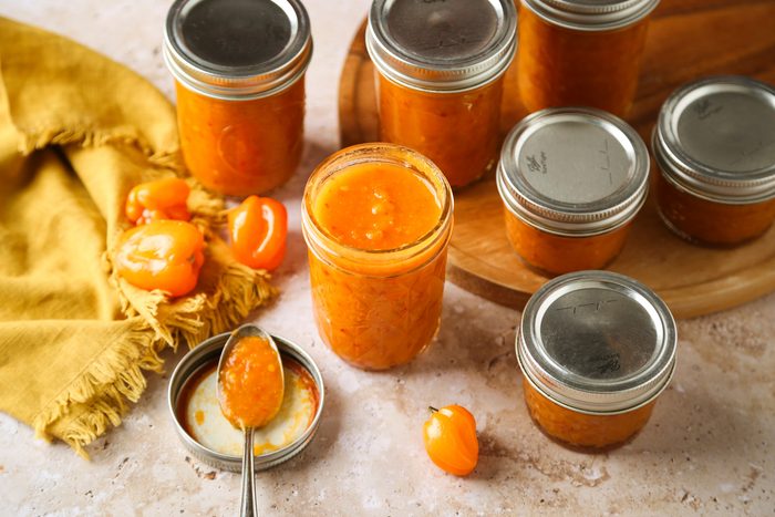 High angle view shot of Homemade Spicy Hot Sauce; stored in jars; round wooden board; yellow napkin; marble surface;