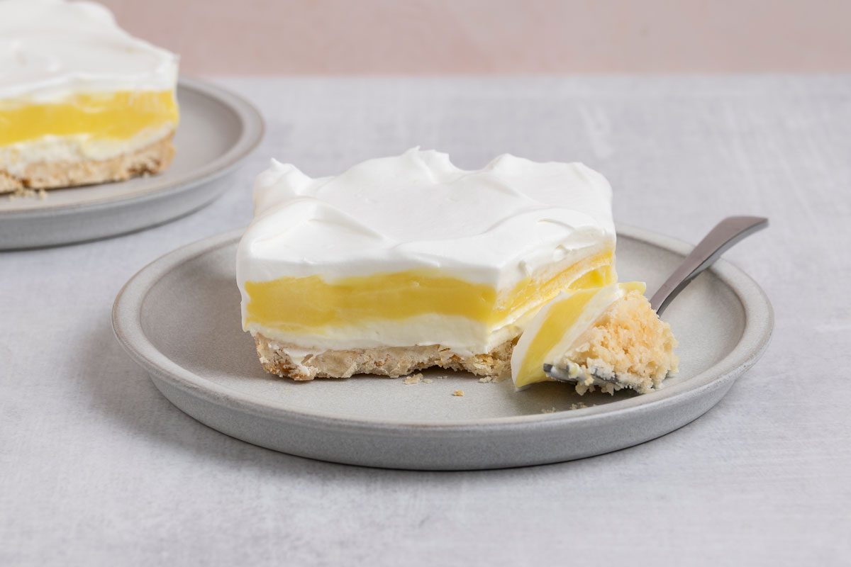 horizontal shot of a slice of Lemon Lush presented on a pale, round plate; on which a fork rests