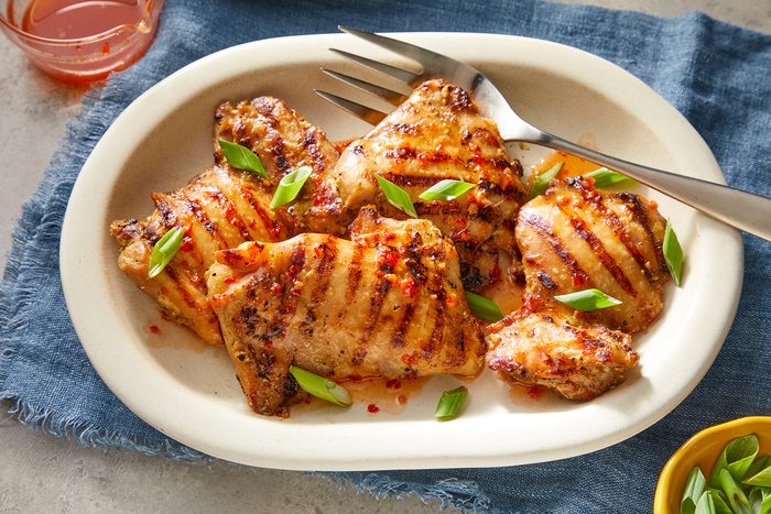 Grilled chicken pieces on a white plate, garnished with chopped green onions.
