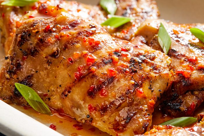 Grilled chicken pieces on a white plate, garnished with chopped green onions.