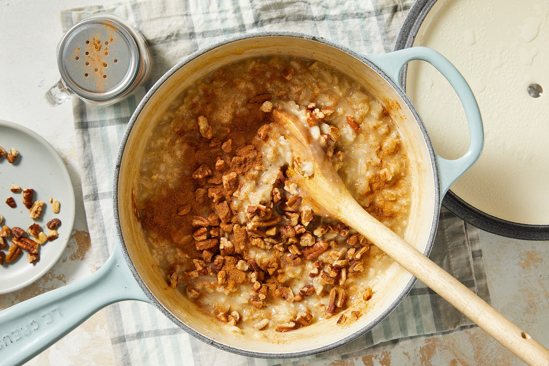 A pot of oatmeal topped with chopped pecans and cinnamon, with a wooden spoon resting inside.