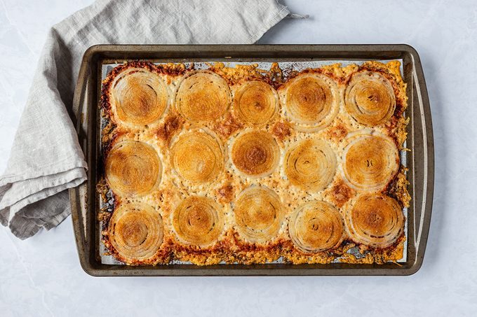 A baking sheet topped with golden-brown circular slices of bread, each surrounded by a crispy cheese crust. A light-colored cloth is draped over one corner of the sheet.