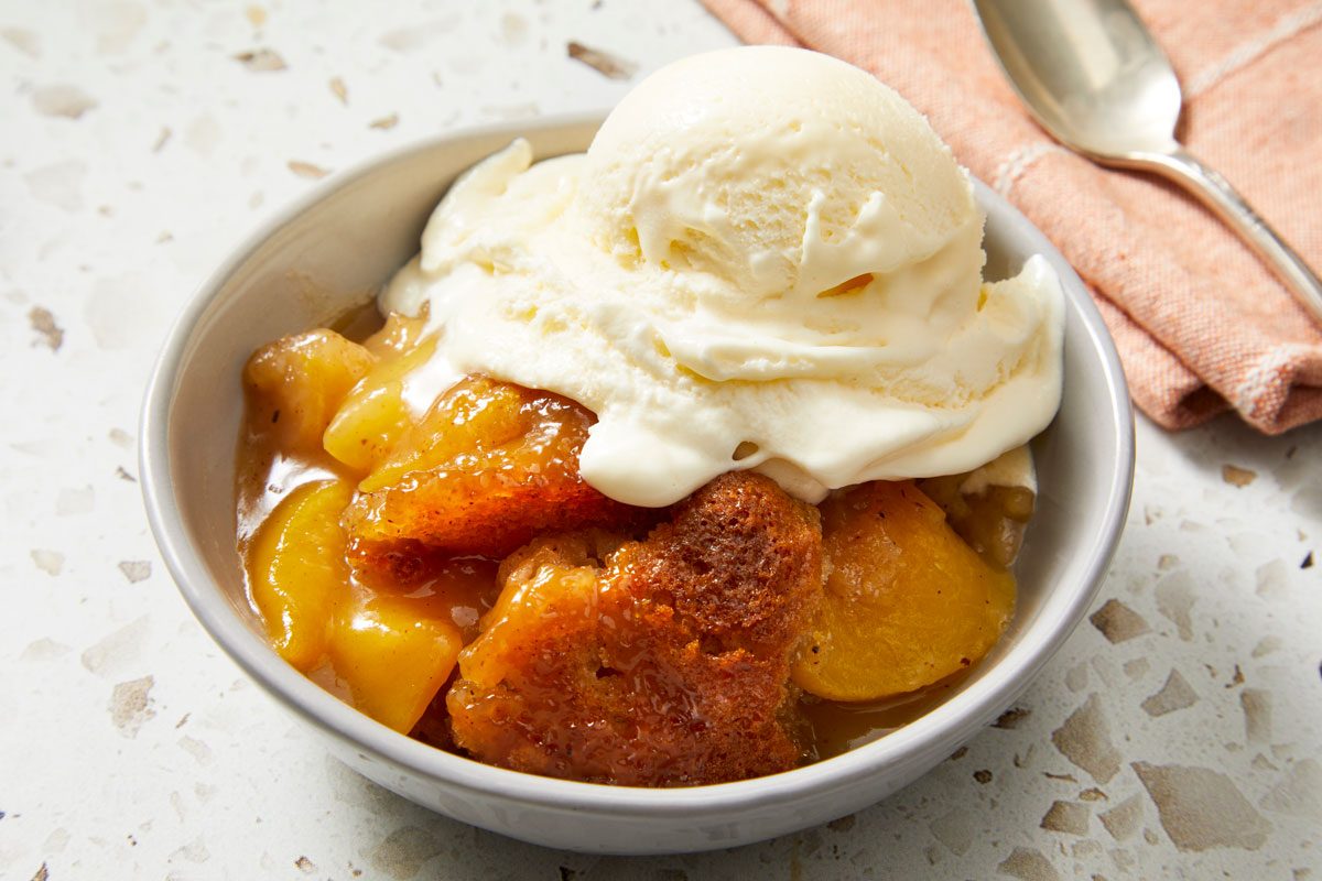 Close-up shot of Tennessee Peach Pudding; served in a bowl top with ice cream; a spoon rest on a napkin nearby; all set on a marble surface;