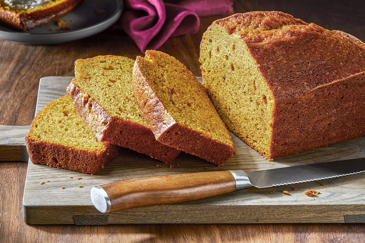 Pull shot of a fresh loaf of pumpkin spice bread, which is golden brown in color. A few slices have been cut from the loaf.