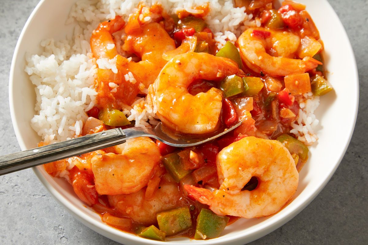 3/4th shot of a white bowl of Spicy Shrimp with Rice; a silver spoons lay on the dish;