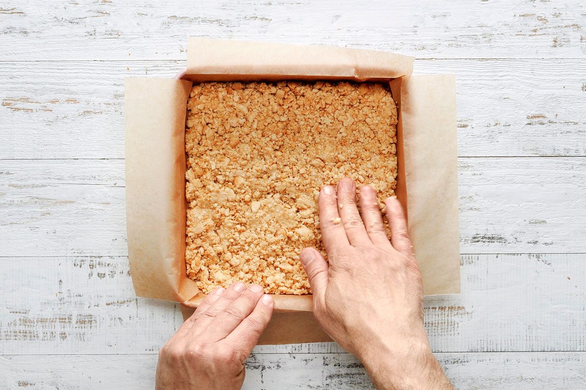 Overhead shot; In a small bowl mix cookie crumbs and butter; Press onto bottom of prepared pan; Bake until firm 15-20 minutes; Cool on a wire rack; white wooden surface;
