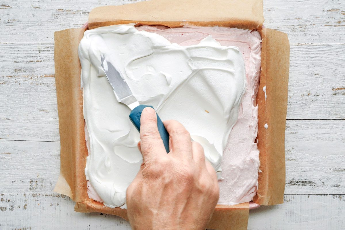 Overhead shot of top again whipped topping; freeze; covered; until firm; cake knife; white wooden surface;
