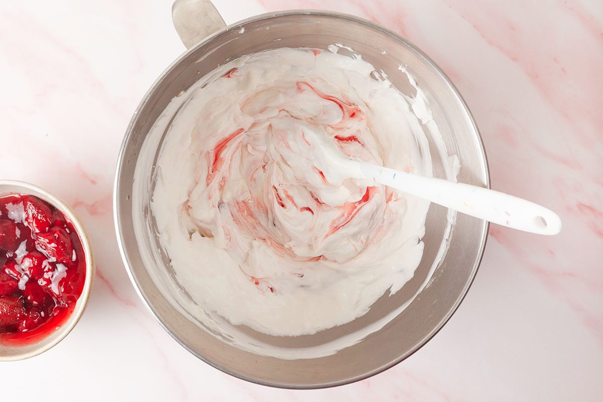 Cream cheese, sugar and strawberry pie filling being mixed in a mixing bowl