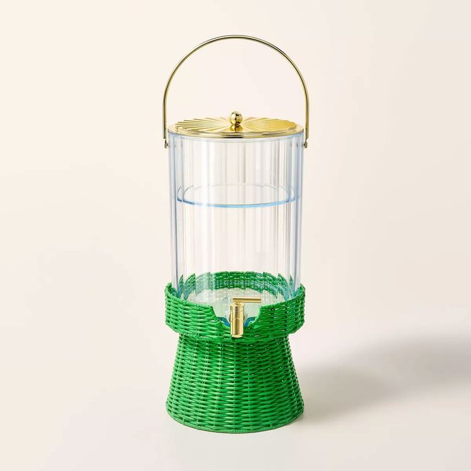 Acrylic beverage dispenser with a green wicker base on a tan background