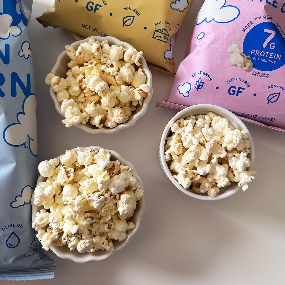 Three cups of Khloud popcorn with bags in the background