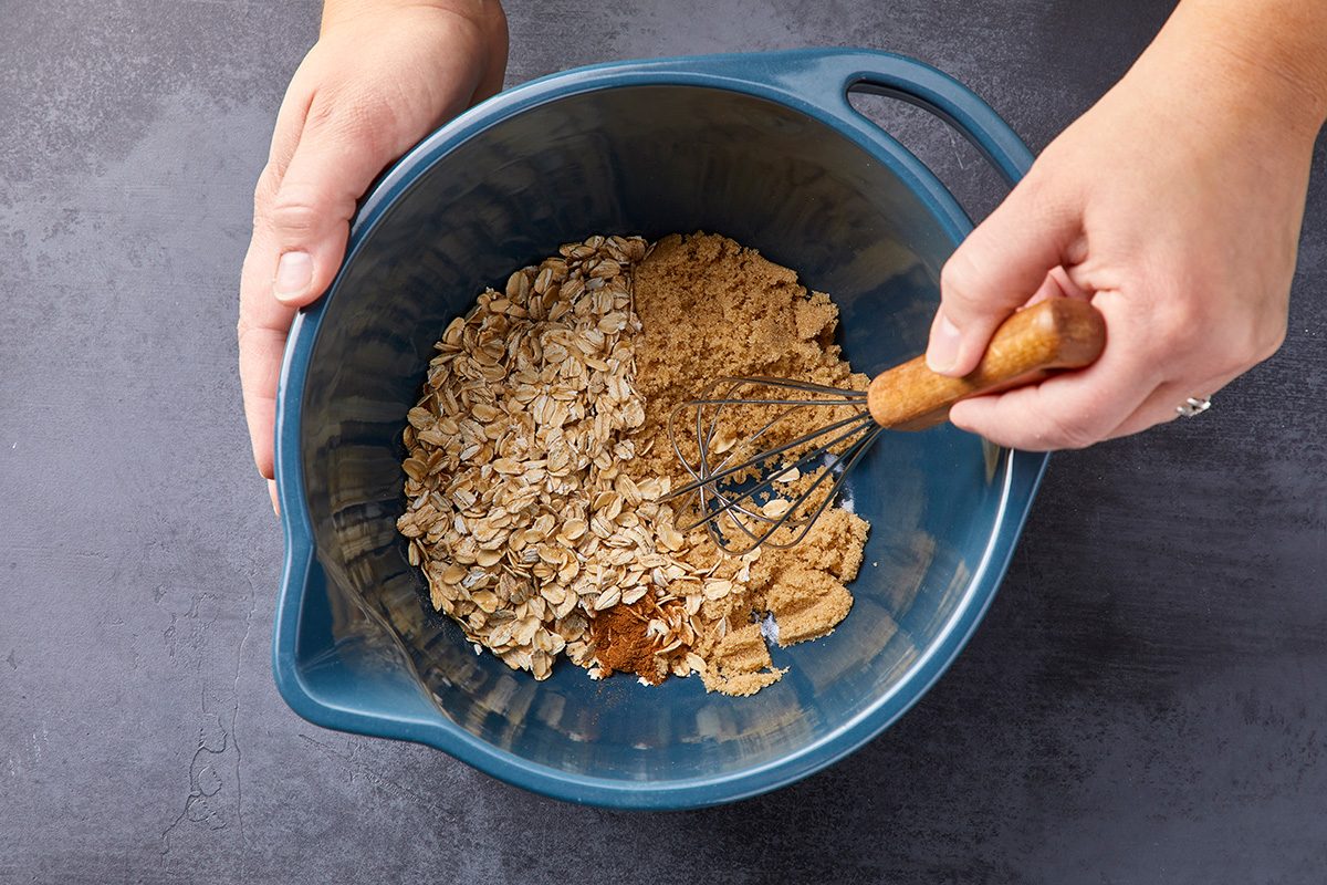 Overhead shot of a small bowl whisk together oats; brown sugar; and cinnamon; dark surface
