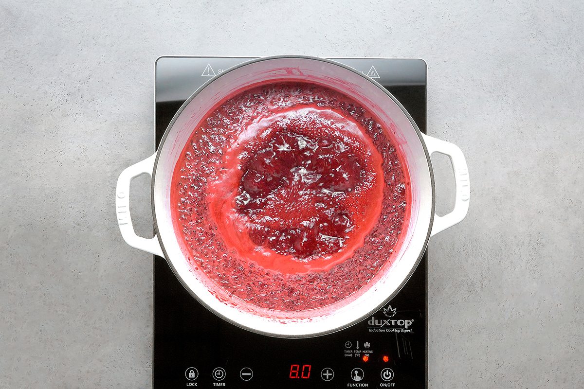 A pot of red liquid boiling on an electric stovetop, viewed from above. The stovetop display shows the temperature set to 80°C.