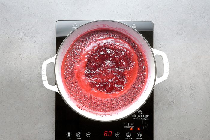 A pot of red liquid boiling on an electric stovetop, viewed from above. The stovetop display shows the temperature set to 80°C.