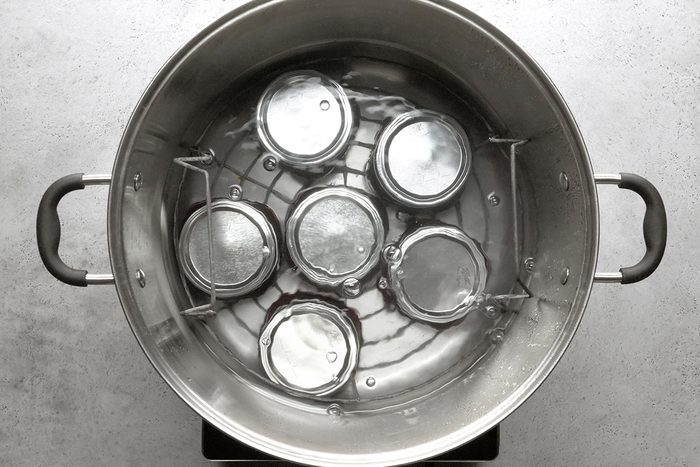 A large metal pot filled with water contains six glass jars with metal lids placed upside down inside on a metal rack, ready for processing or sterilizing.