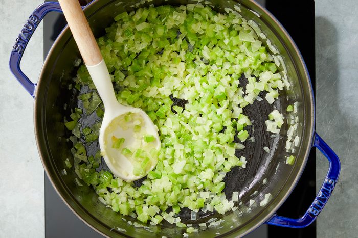 Overhead shot of a large saucepan; melt butter over medium heat; add onion and celery cook until tender 4-5 minutes; spoon; induction; grey surface;