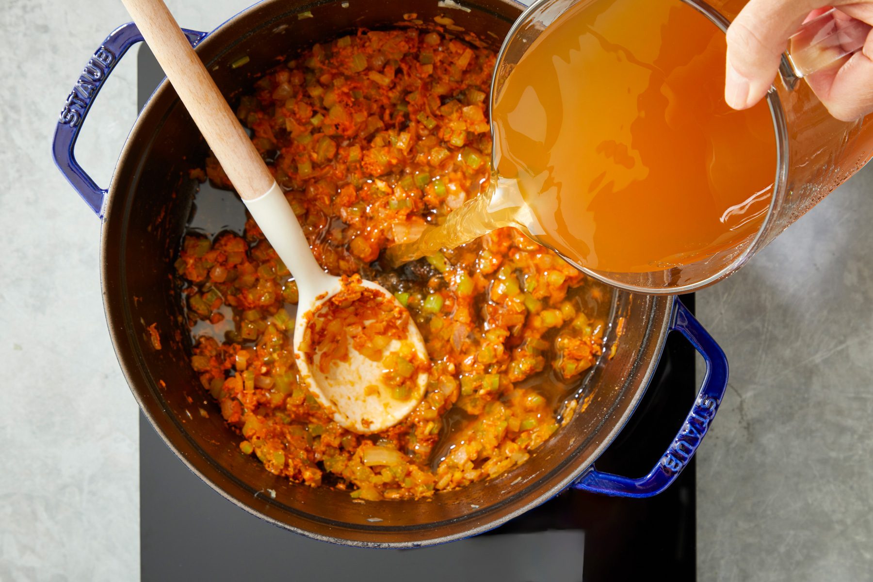Overhead shot of gradually add seafood stock until well combined; add crab and bay leaves; Bring to a boil; induction; spoon; grey surface;