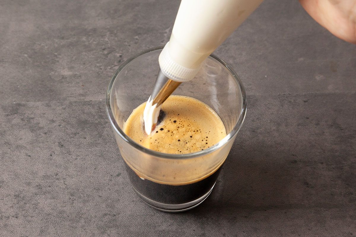 Pour espresso into a mug. Carefully pipe the whipped cream on top.