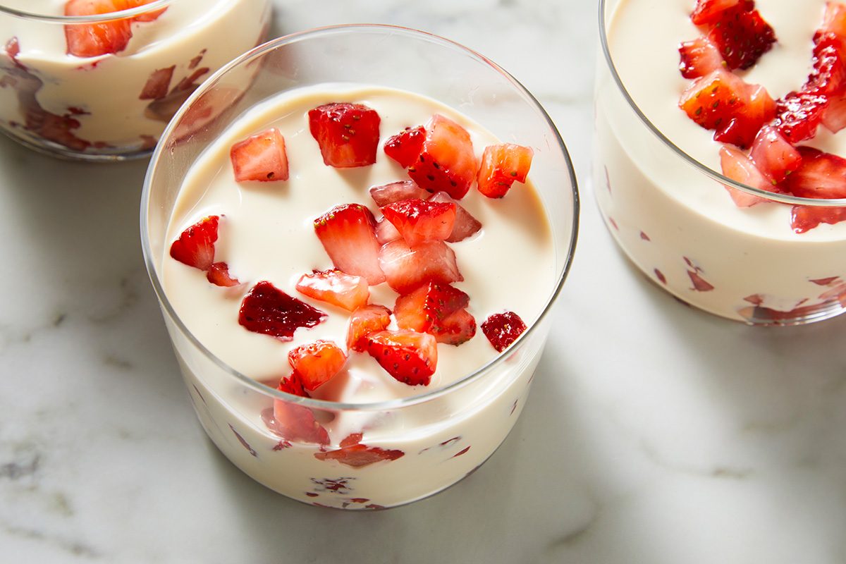 Three clear glasses filled with creamy dessert topped and mixed with chopped fresh strawberries, placed on a white marble surface.