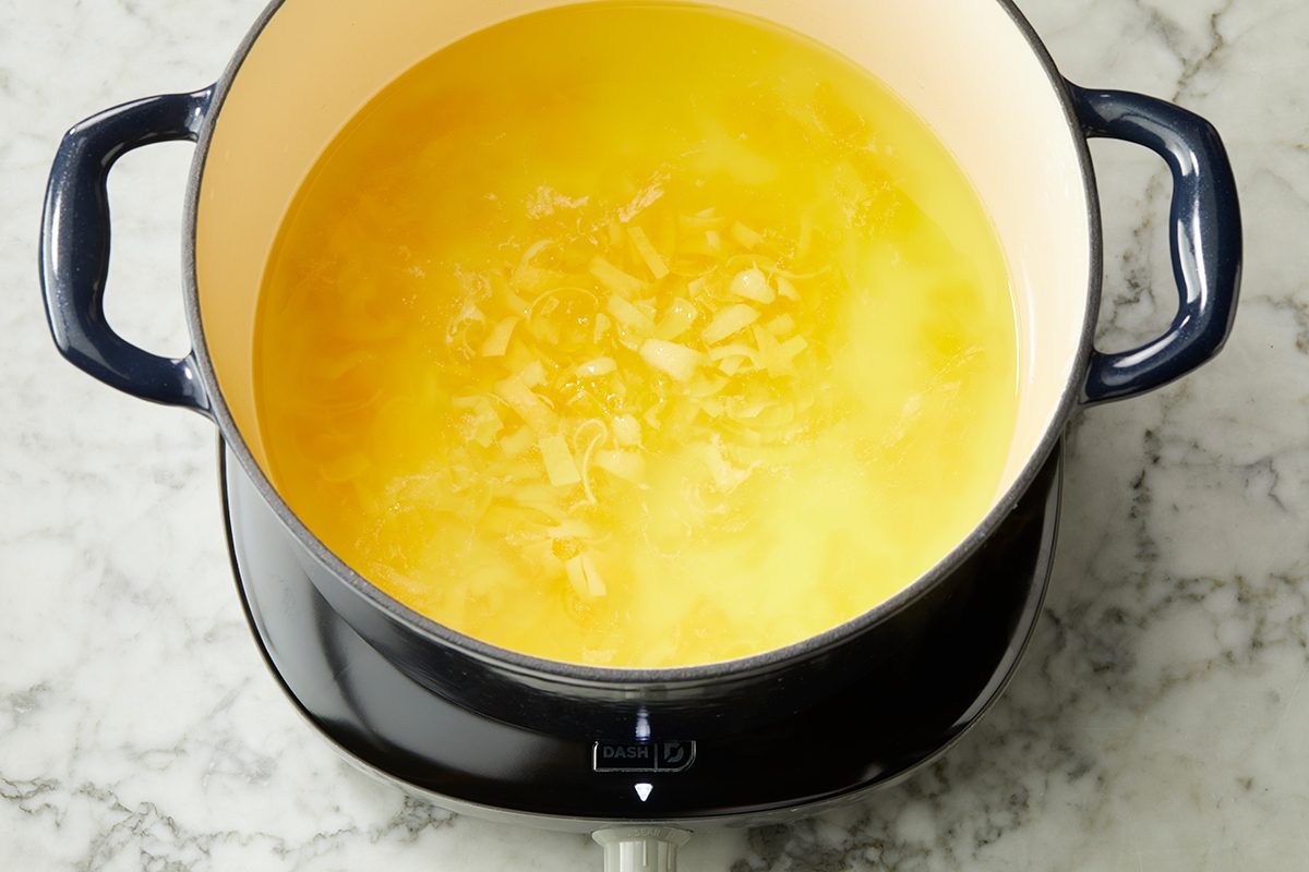 A pot filled with melted butter and bits of onion sits on a stovetop, ready for cooking on a marble countertop.