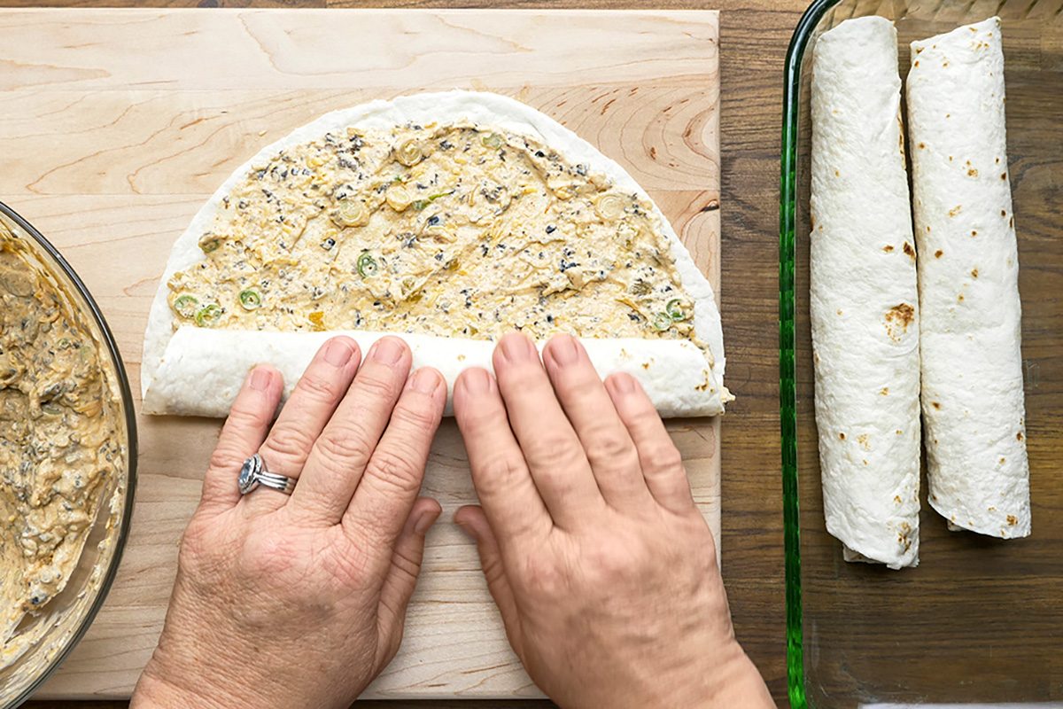 Overhead shot of roll up jelly-roll style; cover and refrigerate for 2 hours or overnight; wooden board; placed on glass baking pan