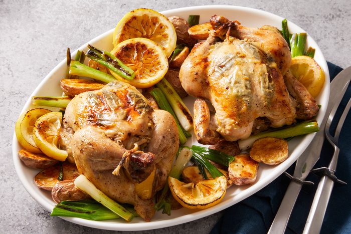 Roasted Cornish Game Hen served on a white plate with some vegetables and silverware kept on side