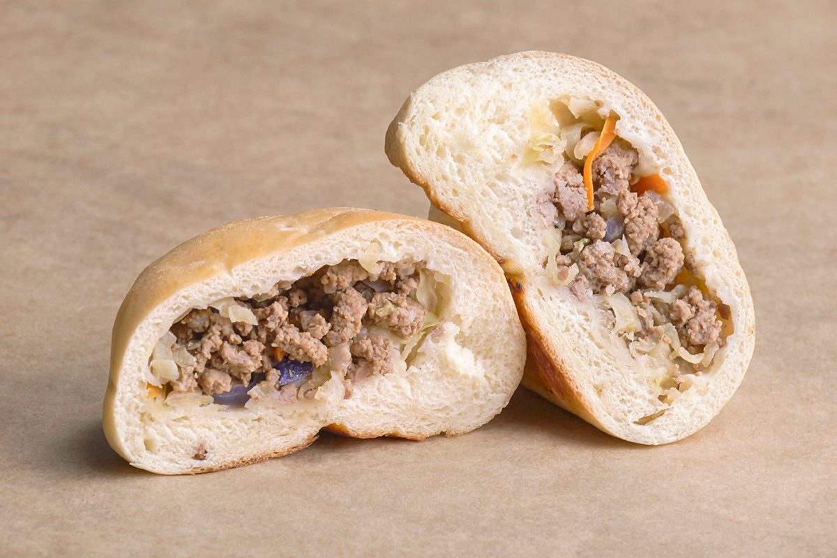 A baked bread roll sliced in half, revealing a savory filling of ground beef and diced vegetables on a neutral background.