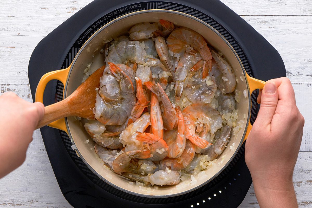 A cook mixing shrimp in a pot, emphasizing the process of preparing a seafood dish.