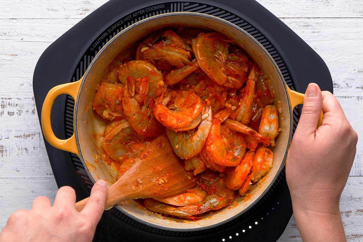 A person using a spoon to stir a pot of food, engaged in meal preparation.