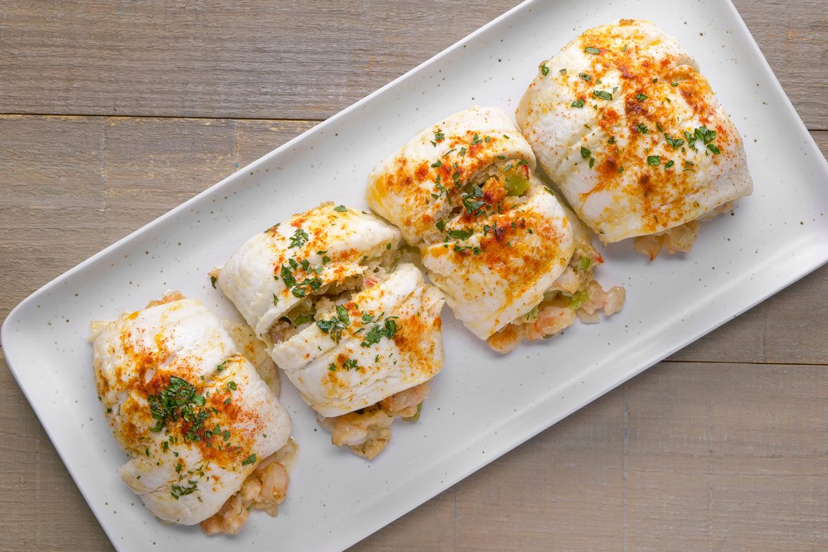 overhead shot of Shrimp Stuffed Flounder presented on a rectangular white plate; the dish consists of several pieces of flounder fillet that are neatly rolled or folded; the background is a wooden surface