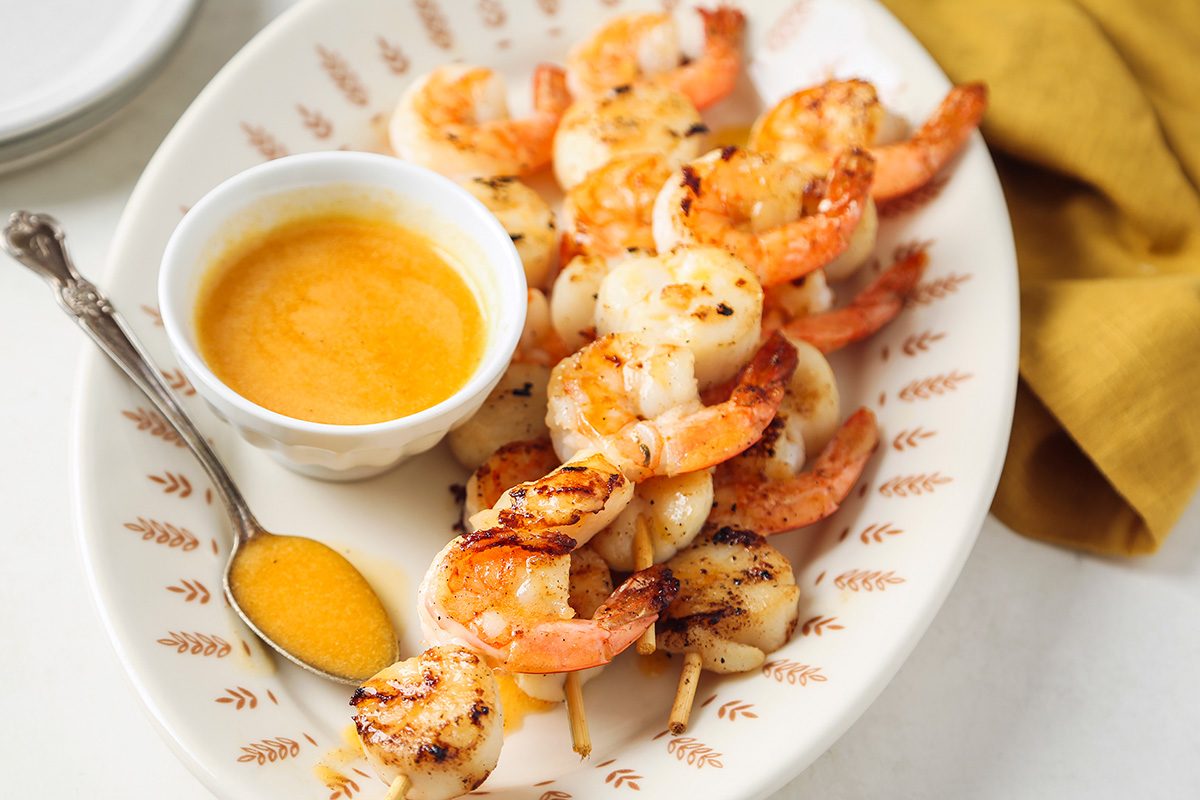 Grilled shrimp skewers drizzled with a vibrant orange marmalade sauce, served on a white plate.