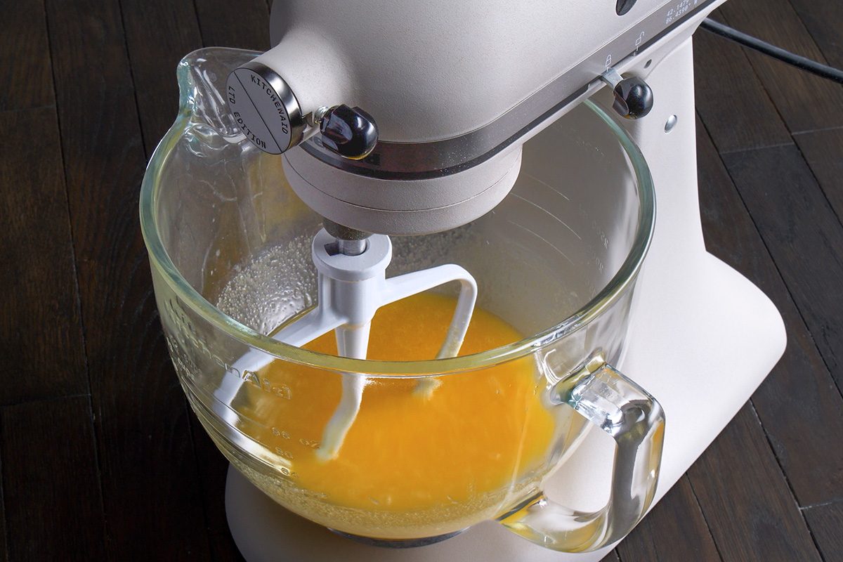 3/4th shot of a stand mixer with glass mixing bowl that is partially filled with a vibrant yellow mixture