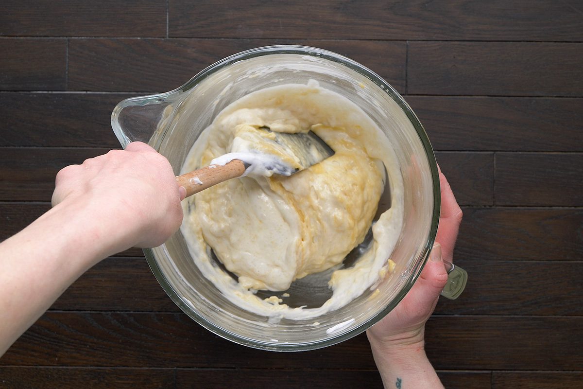 overhead shot of a person is seen mixing a creamy batter in a glass mixing bowl
