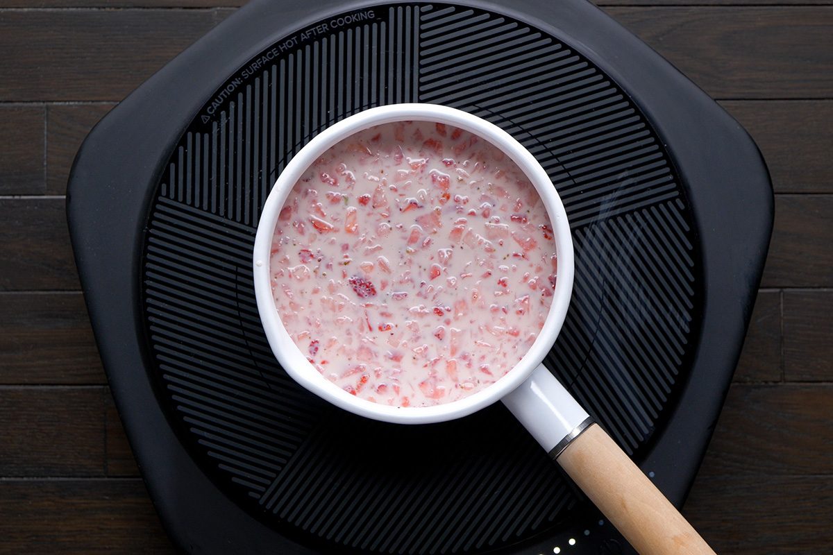 overhead shot of a white saucepan filled with a light pink mixture containing small pieces of strawberries