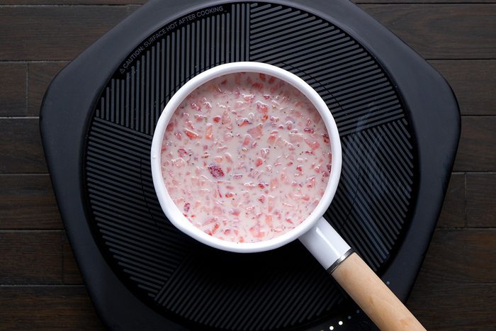 overhead shot of a white saucepan filled with a light pink mixture containing small pieces of strawberries