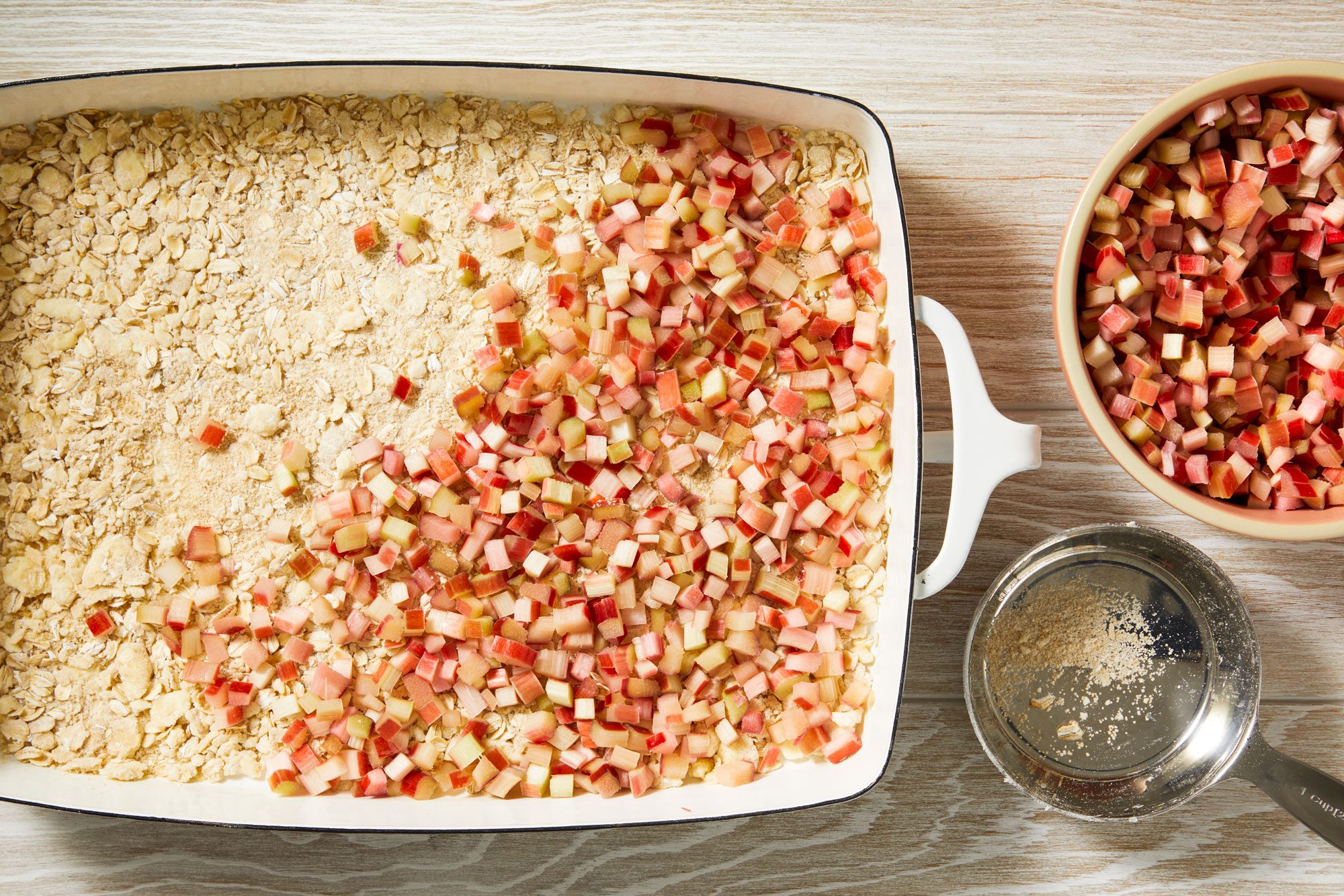 Overhead shot of Pat 2 cups mixture into a greased 13x9-inch baking dish; cover with rhubarb; Set aside remaining crumb mixture; cream wooden surface