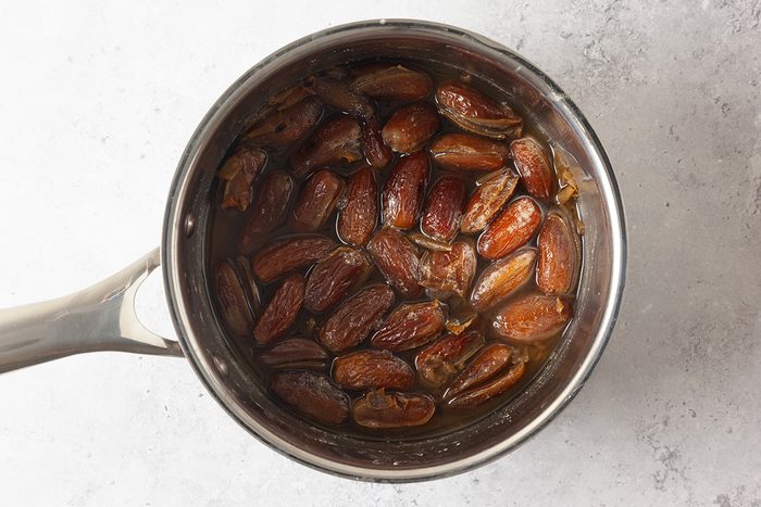 A saucepan filled with whole dates soaking in water, viewed from above on a light-colored surface.