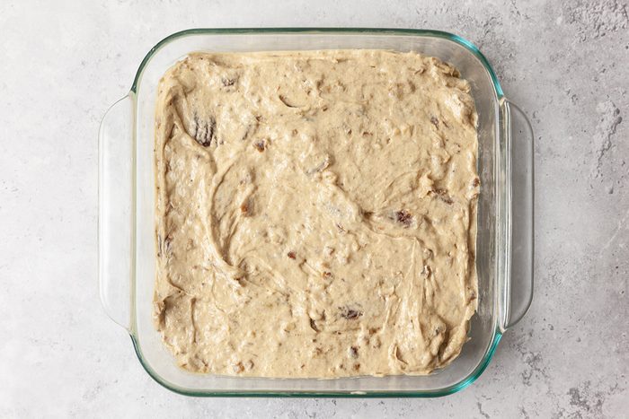 A glass baking dish filled with unbaked cookie dough, spread evenly across the bottom. The dough has a creamy texture with visible chocolate chunks and sits on a light gray countertop.