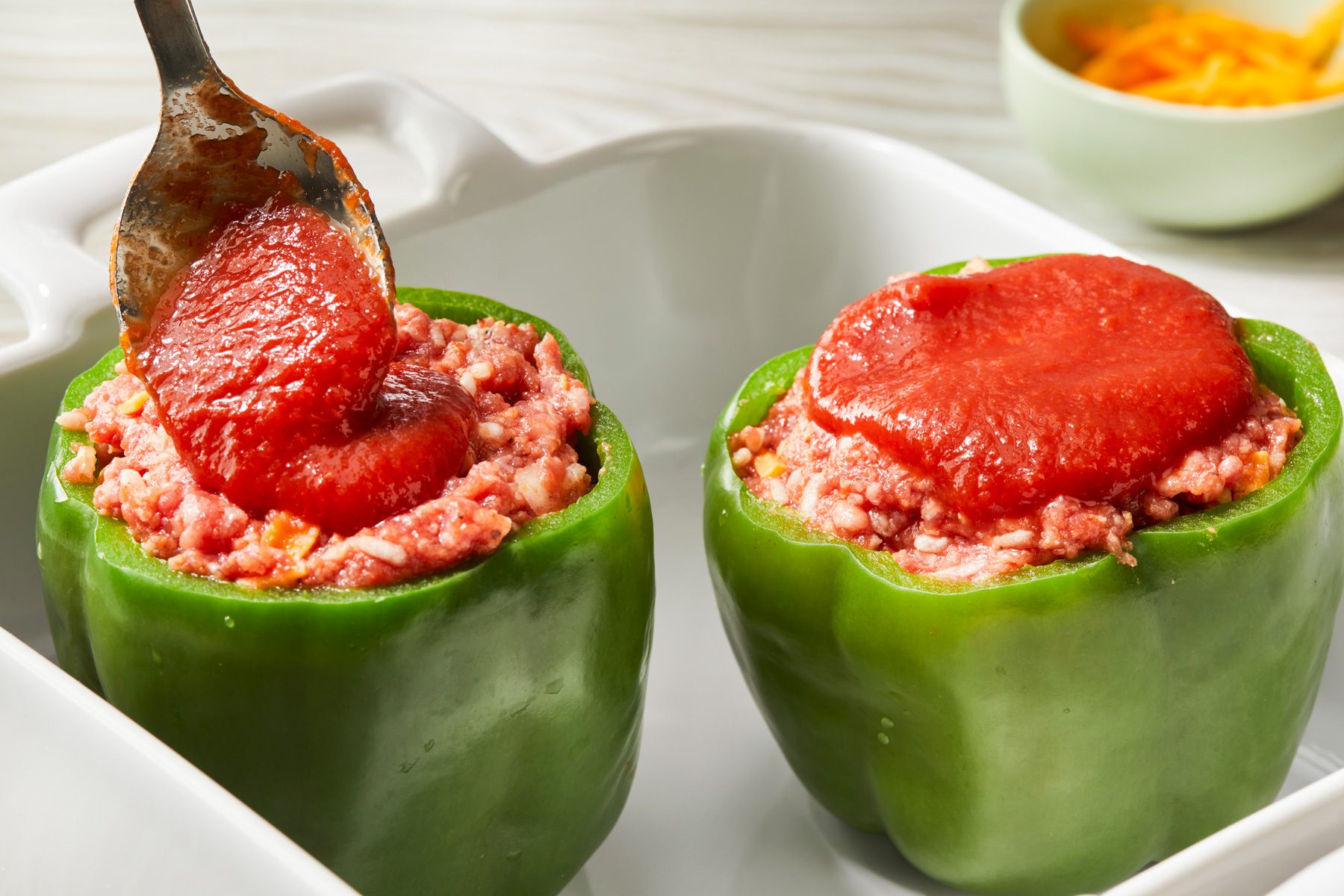 Close-up shot of Pour the remaining tomato sauce over peppers; Cover and bake at 350 degree for 45-60 minutes or until meat is no longer pink and peppers are tender; all set on a cream-colored wooden surface;
