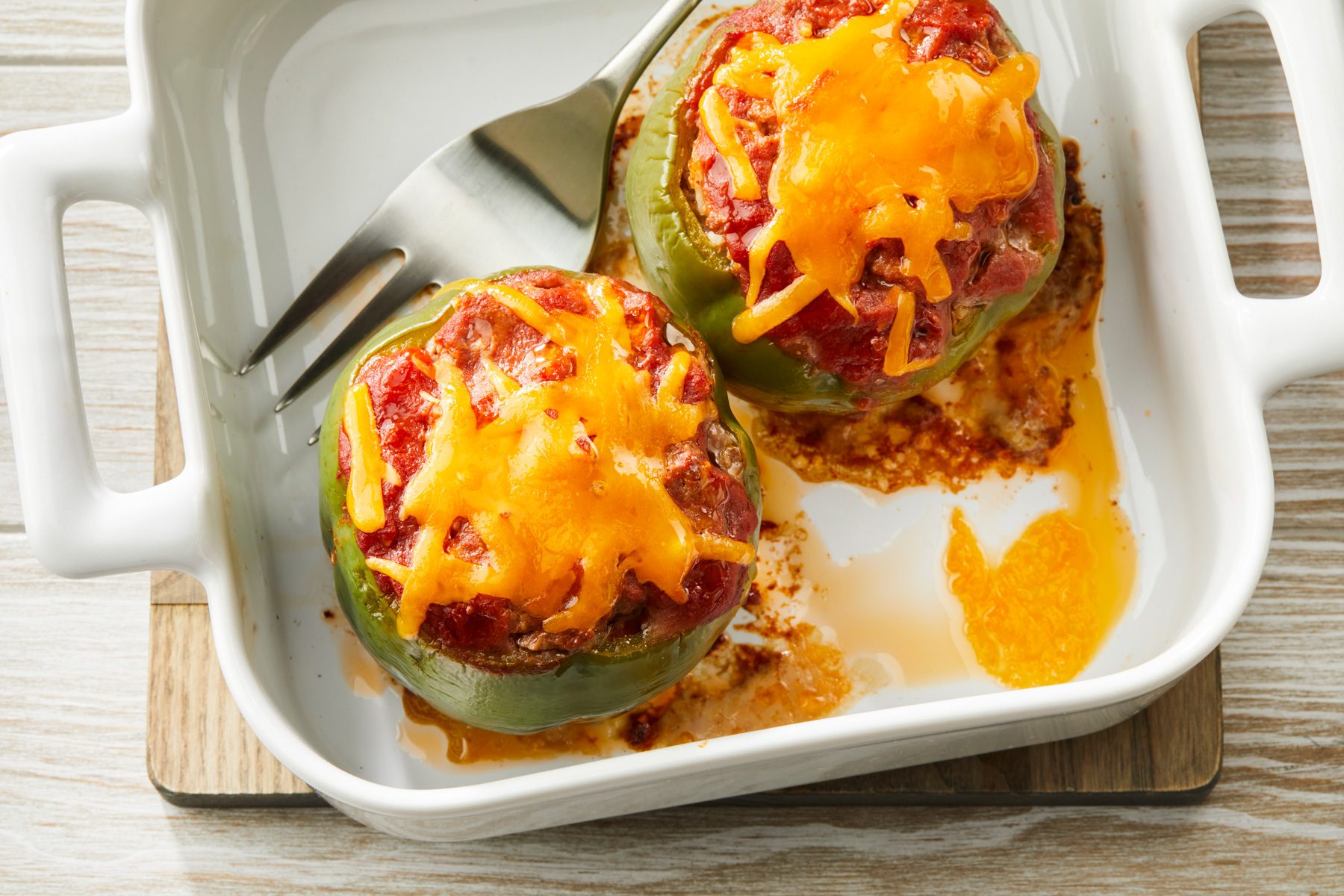 Overhead shot of Stuffed Peppers for Two in a white baking sheet with a fork; placed on a wooden plate; all set on a cream-colored wooden surface;