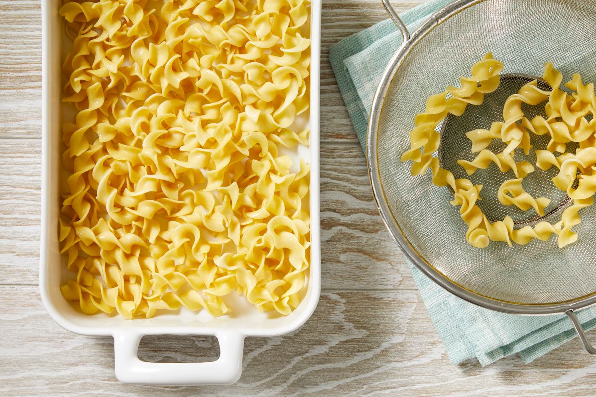 Overhead shot; Preheat oven to 350 degree; Cook noodles according to package directions; Drain noodles; place in a greased 11x7-inch baking dish; a napkin; cream-colored surface;